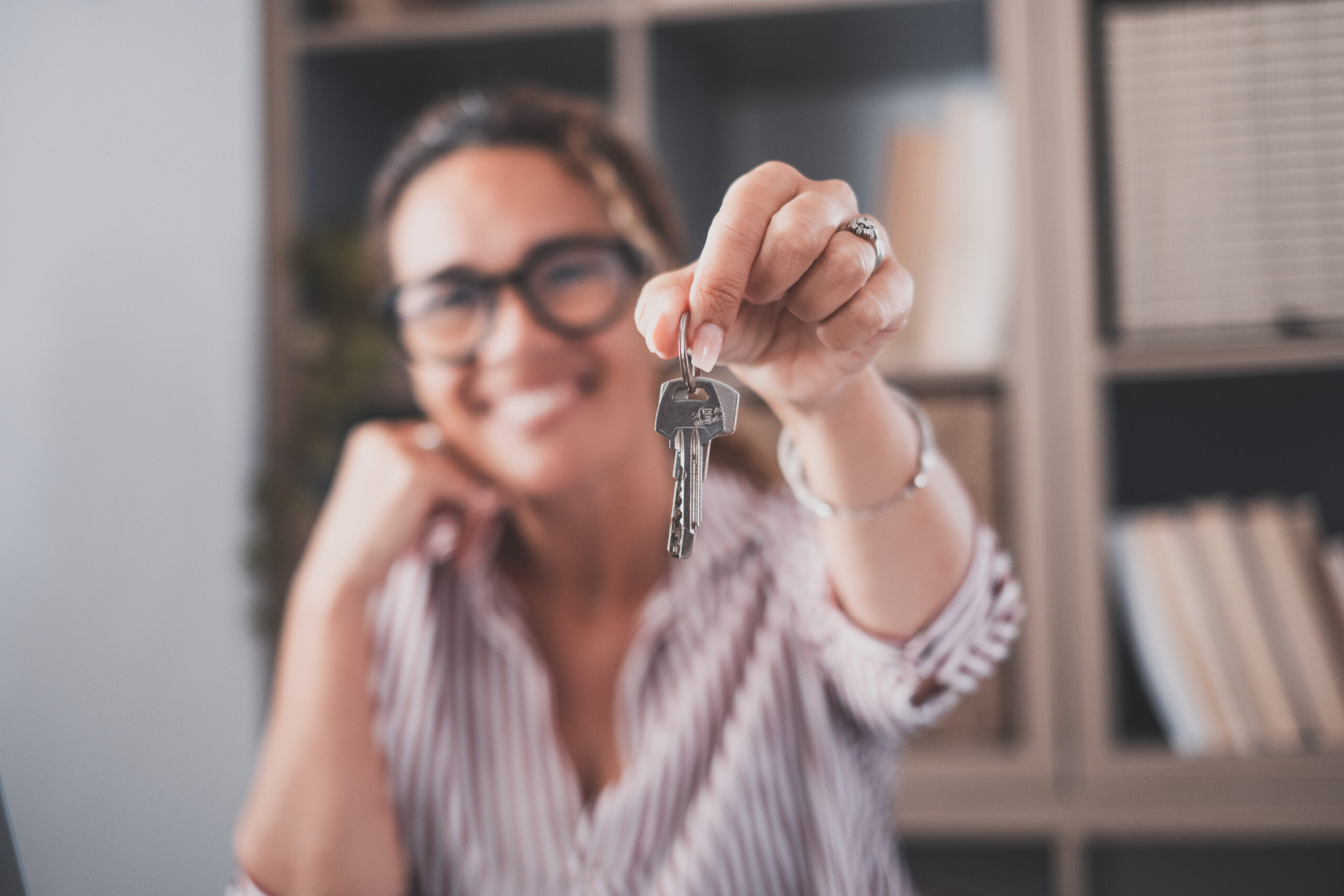 Focus on bunch of keys from house flat apartment in hand of smiling female. Blurred portrait of confident woman professional realtor offering new dwelling real estate unit to potential buyer. Close up university student moving checklist